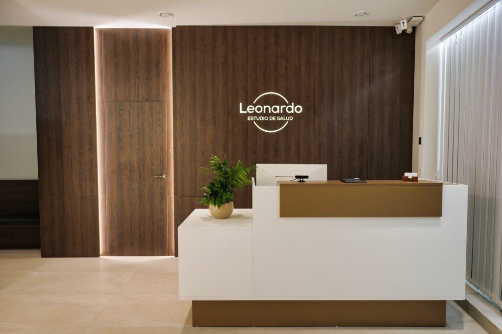 Recepción de la clínica Leonardo Estudio de Salud, con un mostrador blanco y una pared de madera con el logotipo.