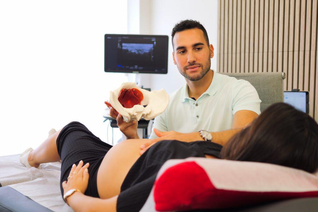 Fisioterapeuta realizando una valoración a una paciente embarazada, explicando la anatomía de la pelvis con un modelo 3D.